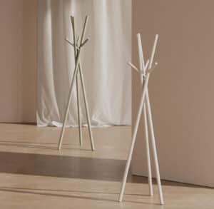 Two white, twig-like sculptures with multiple branches stand in a neutral gallery space against a beige wall and curtain.